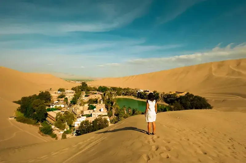 Mujer mirando desde lo alto a la Huacachina en verano en peru